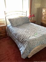 Full view of bed with bedding and pillows on carpeted bedroom floor with nightstand and lamps beside.