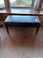 Vinyl upholstered rectangular bench in brown color with grid stitching pattern visible on top, angled photo showing bench against window and carpeted floor.