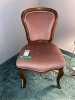 Front view of the vintage wood framed upholstered chair showing pink velvet fabric and curved legs.