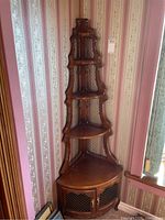 Full view of the wooden corner display shelf in a corner, showing four triangular shelves and the bottom cabinet with mesh doors.