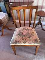 Front view of one wooden dining chair with floral fabric seat, showing wear.