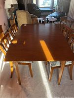 View of the full rectangular dining table with chairs around it showing the wood finish and some scratches.