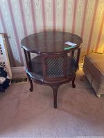 Front view of round wooden end table showing wire mesh inset panels and carved details.