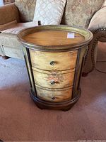 Full view of the oval wooden end table with three curved drawers and floral design on drawer fronts.
