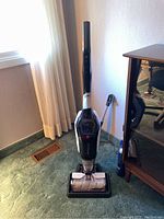 Full view of the Bissell CrossWave Cordless Max standing on green carpet, showing upright floor cleaner and part of the charging base.