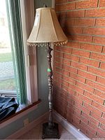 Full view of the floor lamp next to a window and a brick wall, showing its overall height and design.