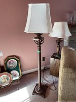 Full view of the floor lamp showing the white pleated fabric shade and ornate metal stem with scrollwork.