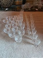 Overview of multiple rows of various cut crystal glasses including champagne, wine, and aperitif glasses arranged systematically on carpet.