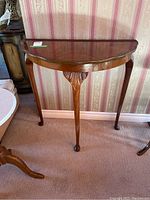 Front view of a vintage semi-circular three-legged wooden side table with carved details.