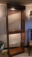 Front view of vintage mid century modern display shelving with light on top, wood frame, and glass shelves.