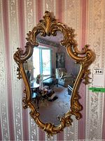 Front view of ornate wall mirror showing detailed gold-toned scrollwork frame and vintage mottled glass.