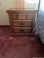 Front view of one Palliser nightstand showing three drawers with brass handles and knobs, wood grain finish, on a carpeted floor.