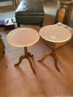 Pair of round occasional tables with marble tops, showing the two matching tables on carpeted floor.