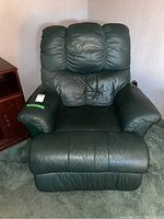 Front view of green leather recliner chair showing padded segmented backrest and plush cushioned armrests, with some creasing in leather upholstery.