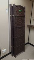 Two matching brown woven wicker room dividers folded and standing upright against the wall.