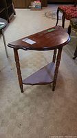 Angled side view of vintage wood side table showing semi-circular top, turned legs, and lower shelf.