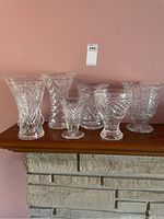 Seven clear cut glass crystal vases displayed on a wooden surface, varying in size and ornate patterns.