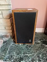 Front view of one vintage wooden cabinet PSB speaker with black fabric grille and label.