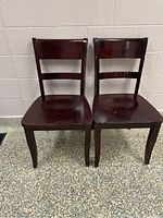 Pair of two dark brown wooden kitchen chairs placed side by side showing full front view.