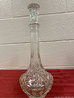Full view of the clear glass decanter showing the tall slender neck, wide bottom with pinwheel cut pattern, and stopper on top.