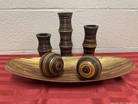 Photo showing four wooden candle holders with multi-tone circular designs placed on an elongated wooden tray, all set on a red tablecloth.