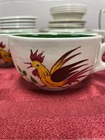 Close-up of white ceramic cup with green rim and colorful rooster motif