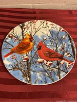 Front view of the decorative ceramic plate featuring two cardinals on snow-covered branches with blue sky background.