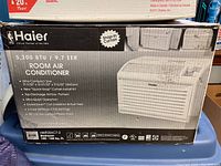 Box front view showing Haier branding, 5200 BTU cooling capacity, 9.7 EER, and features like ultra-quiet operation, snap-in curtain installation, and top-discharge airflow pattern.