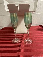 Two green champagne flutes with clear twisted stems in front of a white box on a red tablecloth