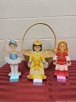 Three wooden magnetic princess dolls standing on individual pastel blocks with wicker basket behind them on a table.