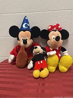 Three plush stuffed toys: large Mickey in sorcerer hat and robe, small classic Mickey, large Minnie in polka dot dress and bow.