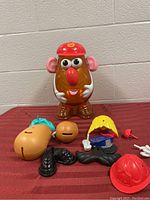 Mr Potato Head storage container and detached facial and accessory pieces on a red cloth.
