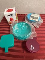 All five Tupperware items together on a striped surface including box, bowls, spatula, and container.