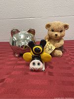 Lot of three piggy banks on red cloth with concrete wall behind