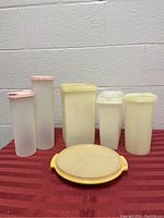 Photo showing all six Tupperware containers including three cylindrical with pink lids, three rectangular with yellow lids, and one round shallow container with yellow lid
