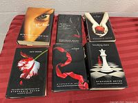 Six hardcover books by Stephenie Meyer including the Twilight series and The Host, displayed stacked and spread on red striped fabric.