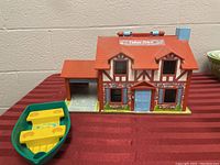 Front view of vintage Fisher Price Quaker Oats playhouse with attached garage and green and yellow boat accessory on side.