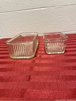 Two vintage clear glass refrigerator dishes on a red striped cloth, showing front and side view.