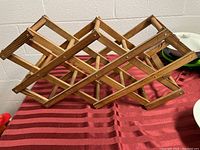 Wooden folding wine rack displayed in an expanded open position on a red striped fabric.