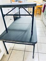 Side and partial top view of two stacked black folding tables showing metal legs and tabletops.
