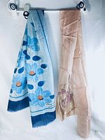 Two long rectangular silk scarves hanging, one pink by Jane Rowan and one blue by Remoy d'Urville, showing full length and design