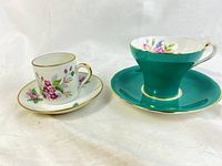 Photo showing both teacups and their matching saucers, highlighting the turquoise Aynsley corset cup and smaller white Limoges demitasse cup with floral designs.