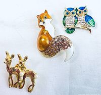 Three animal brooches on white background showing gold-tone twin deer with faux pearl, enamel and rhinestone fox, enamel and rhinestone owls.
