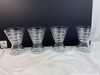 Front view of all 4 Bormioli Rocco waisted ringed glasses in a row on a white surface with black background