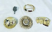 Top front view of 5 brooches including floral, carriage, geometric and bus designs