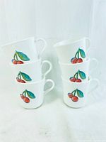 Stack of three white ceramic mugs with cherry design on one side, showing the bright red cherries and green leaves