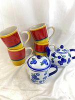Stack of four colorful Royal Norfolk Mambo pattern mugs with two April Cornell Blueberry pattern ceramic pieces - teapot and lidded mug