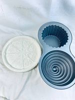 Photo showing both the ceramic cookie mold with heart and flower designs next to the Wilton giant cupcake pan with multiple cavities.