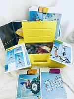 Photo of open yellow K'nex plastic storage case with multiple instruction booklets displayed around the case and visible pieces inside.