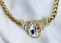 Close-up of the necklace's central crystal pendant and adjacent set crystal details on the gold-tone braided chain, highlighting the sparkling clear crystals and smooth metal finish.